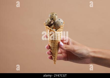 Hand holding waffle cone filled with quail eggs.on beige background. quail farm concept Stock Photo