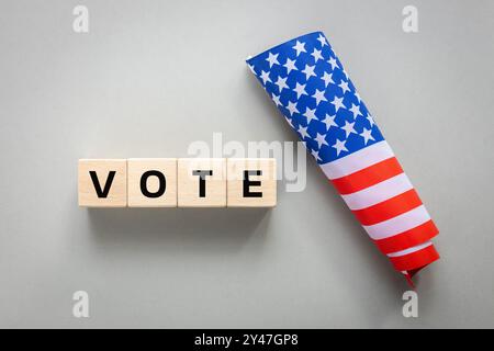 vote 2024, American flag and written word vote on wooden blocks. Gray background, flat lay Stock Photo