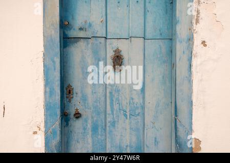 Old wooden door of colonial period house with peeling blue paint and rusty metal knocker and keyhole. Stock Photo