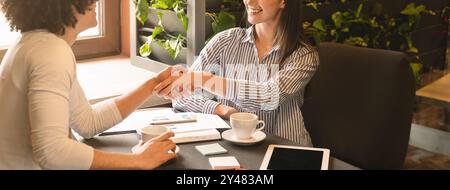 Young colleagues handshaking during informal meeting in cafe Stock Photo
