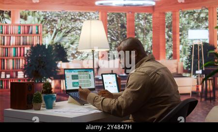 Entrepreneur using a card to make an online shopping payment via electronic banking, purchasing things to help the startup activity. Business owner makes a payment at his home office. Camera B. Stock Photo