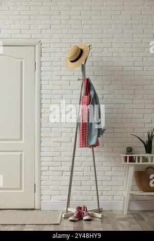 Metal rack with clothes and straw hat in hallway Stock Photo - Alamy