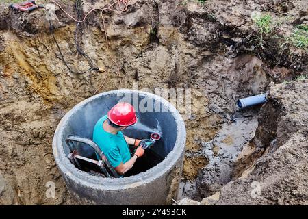 Homeowner uses diamond circular saw to create hole for sewer pipe while installing septic tank. Stock Photo