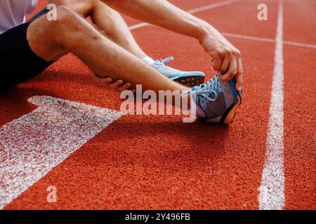 Athlete stretching on a running track, focusing on legs and shoes. Stock Photo