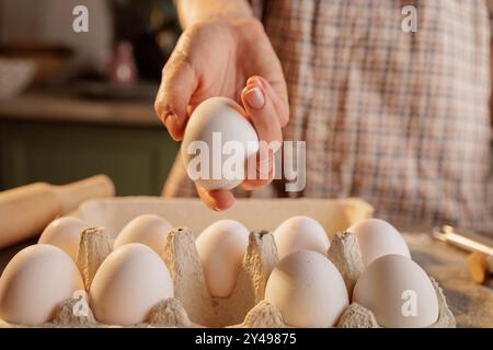 Heart-shaped frying pan for scrambled eggs with broken egg on kitchen table background, cardboard box with eggs and several broken eggshells lie on th Stock Photo