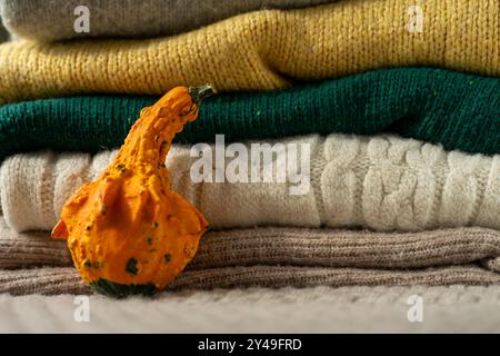 Orange pumpkin near a stack of knitted sweaters on a knitted blanket. Stock Photo