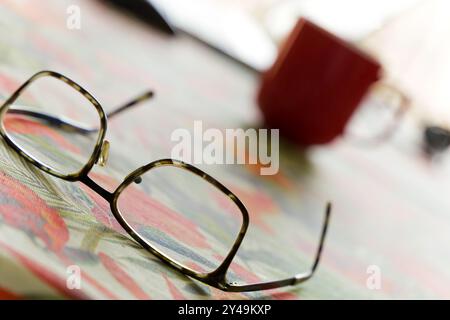 A pair of glasses sits on a table next to a red coffee cup. Concept of relaxation and leisure Stock Photo