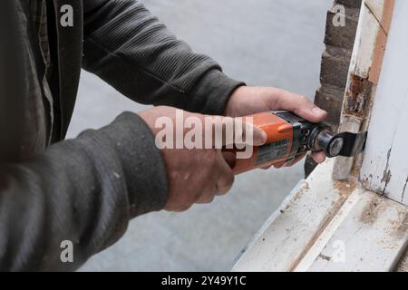 Carpenter cuts a piece of rotten wood from a window frame with an oscillating renovator saw, the unique system for remodeling and renovation Stock Photo