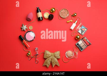 Frame of makeup products and Christmas decor on red background, flat lay. Space for text Stock Photo