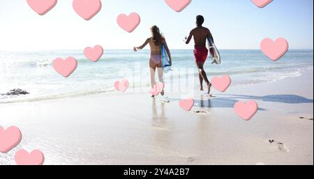 Image of pink hearts over diverse couple running with surfboards on beach Stock Photo
