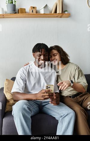 Two men embrace each other while smiling at their phone, enjoying a tender moment together. Stock Photo