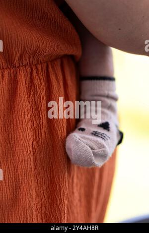 A portrait of the cute leg and foot of a baby wearing a cosy sock pressed safely against the caring mother who is carying the small child. Stock Photo