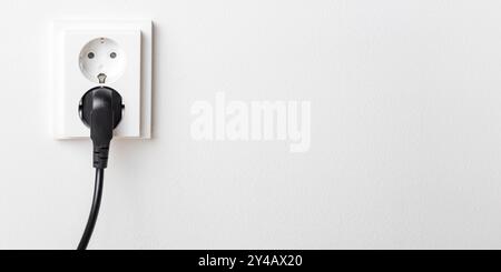 A close-up of a double electrical outlet mounted on a white wall, with a power cord plugged into one of the sockets. Mindful of electricity consumptio Stock Photo