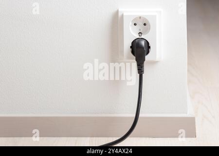 A close-up of a double electrical outlet mounted on a white wall, with a power cord plugged into one of the sockets. Mindful of electricity consumptio Stock Photo