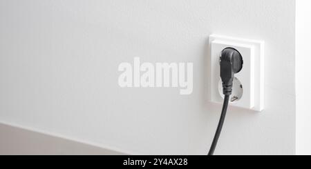 A close-up of a double electrical outlet mounted on a white wall, with a power cord plugged into one of the sockets. Mindful of electricity consumptio Stock Photo