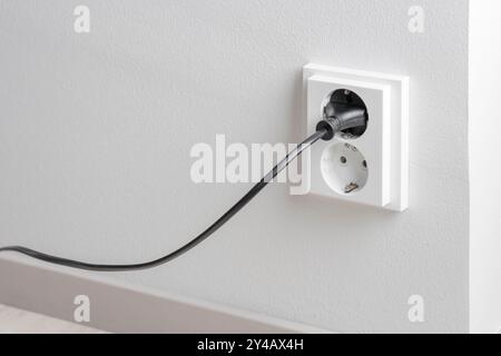 A close-up of a double electrical outlet mounted on a white wall, with a power cord plugged into one of the sockets. Mindful of electricity consumptio Stock Photo