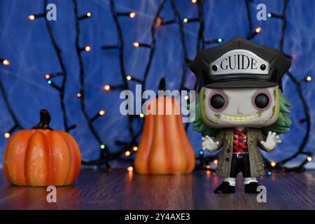 Funko Pop action figure of Beetlejuice from Tim Burton comedy horror film. Blue foggy background, colorful lights, Halloween pumpkins, spider web. Stock Photo