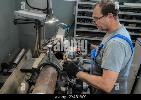 An industrial technician in an organized workspace, using precision tools to work on a piece of metal held in a lathe machine, demonstrating extensive skill and technique. Stock Photo