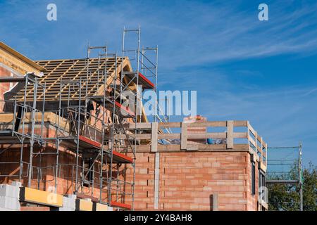 A construction site displays scaffolding attached to brick walls. Workers are engaged in building processes, highlighting the ongoing construction act Stock Photo