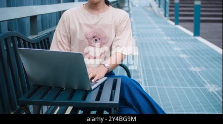 Confident female entrepreneur sits on a metal table next to the corridor in a modern city, She working with laptop computer and online marketing servi Stock Photo