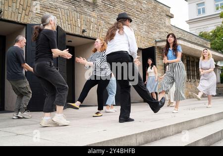 Cheerful dance party outdoors, featuring individuals of different ages enjoying the festive ambiance under illuminated string lights. They are dancing Stock Photo