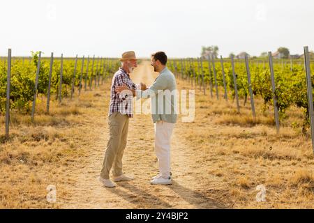 Two men share a meaningful discussion amidst rows of grapevines, enjoying the warmth of the late afternoon sun, symbolizing connection and tradition i Stock Photo