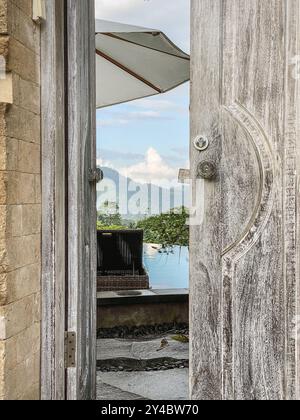 Wooden door slightly open to villa with pool and mountain view, Bali Stock Photo