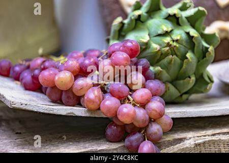 Market stall with red grapes and artichokes on a rustic wooden board Stock Photo
