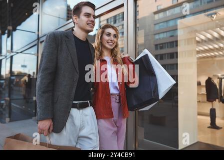 Beautiful couple with shopping bags is talking and smiling while doing shopping in the mall focus on the woman Stock Photo