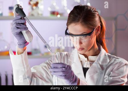 Life scientists researching in laboratory. Focused female life science professional pipetting solution into the glass cuvette. Lens focus on researcher's eyes. Healthcare and biotechnology concept. Stock Photo