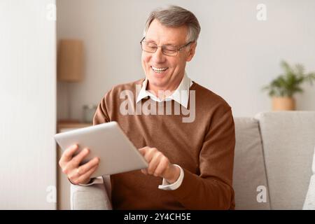 Senior Man With Tablet Computer Browsing Internet Sitting On Sofa Stock Photo
