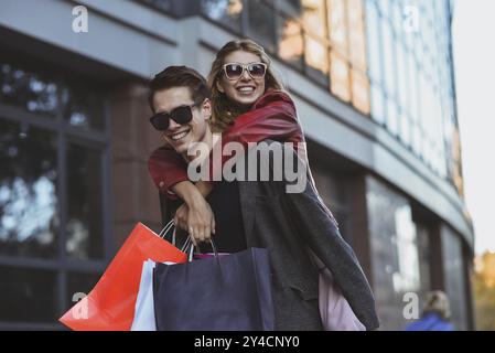 Happy couple shopping together and having fun. Boyfriend carrying his girlfriend on the piggyback Stock Photo
