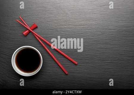 Red wooden chopsticks and bowl of soy sauce on black slate Stock Photo