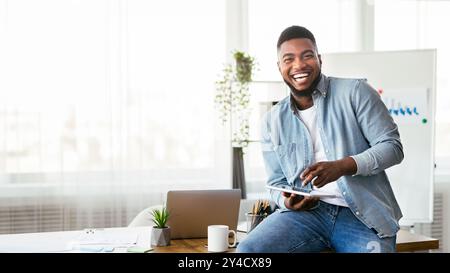 Cheerful black employee using digital tablet in office and laughing Stock Photo