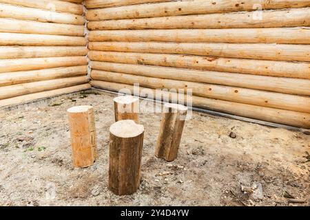 Four logs stand on the earthen floor in empty interior of a new wooden house made of uncolored natural pine tree logs, background photo. Log house is Stock Photo