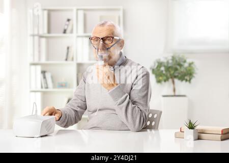 Senior man sitting at home and using a nebulizer Stock Photo