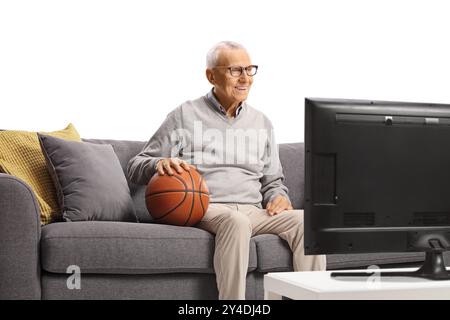 Elderly man with a basketball sitting on a sofa and watching tv isolated on white background Stock Photo