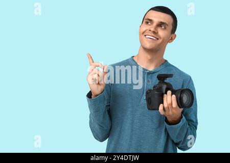 Male photographer with modern camera pointing at something on blue background Stock Photo