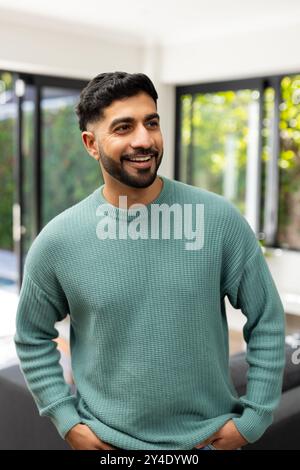 Smiling indian man in green sweater standing indoors with hands in pockets Stock Photo