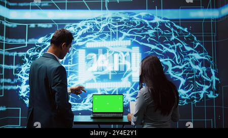 Startup coworkers looking over charts, using AI software on mockup laptop to take data driven decisions. Teamworking colleagues developing artificial intelligence solutions for company, camera B Stock Photo