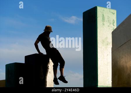 Silhouette of an active young man jumping between concrete blocks practicing parkour, enjoying and exercising, moving freely outdoors. Stock Photo