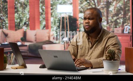 Freelancer managing startup projects and thinking about client needs from his home office, developing new growth strategy. Self employed analyst does telecommuting work on laptop. Camera A. Stock Photo