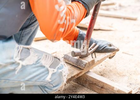 Worker pulling rusty nail out of old pinewood with hammer in construction site. Stock Photo