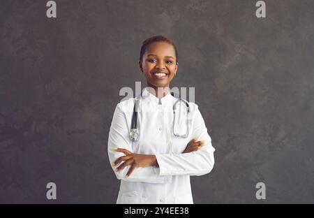 Portrait of confident and proud smiling dark skinned female doctor on gray background. Stock Photo