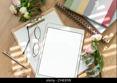 A bright workspace features a blank tablet, an open notebook, stationery tools, and fresh flowers arranged on a wooden table, inviting creativity and Stock Photo