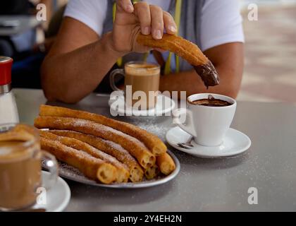 Woman keep pies of  churros in hear hand. Churros popular delicious spanish food with hot chocolate, sugar and coffe on restaurant table Stock Photo