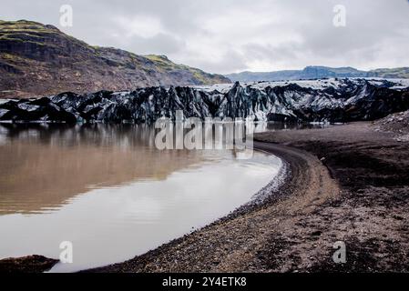 Solheimajokull glacier covered in soot from previous eruptions with the glacial lake descending from the volcano near Vik in Iceland Stock Photo