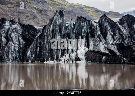 Solheimajokull glacier covered in soot from previous eruptions with the glacial lake descending from the volcano near Vik in Iceland Stock Photo