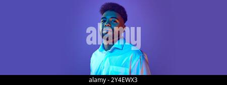 Banner. Young man in white shirt stands confidently, glancing sideways in vibrant neon light against gradient background. Stock Photo