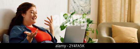 A cheerful young woman with curly hair engages in a lively conversation at home, surrounded by plants and comfort. Stock Photo